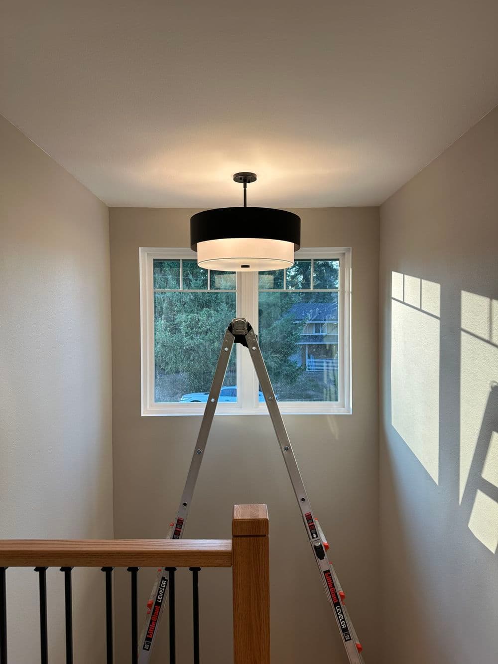Modern ceiling light fixture above a staircase, with a ladder positioned below a window.